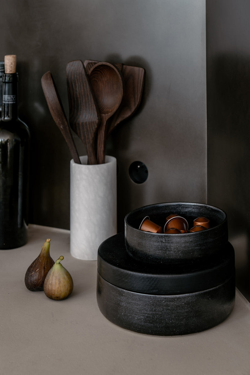 Een set van een albast koker met houten keukengerei en 2 zwarte keramieken potjes met houten deksel verkocht door Anneke Crauwels Home